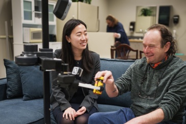 Two people, a young woman and an older man, sit on a couch with a robot in front of them